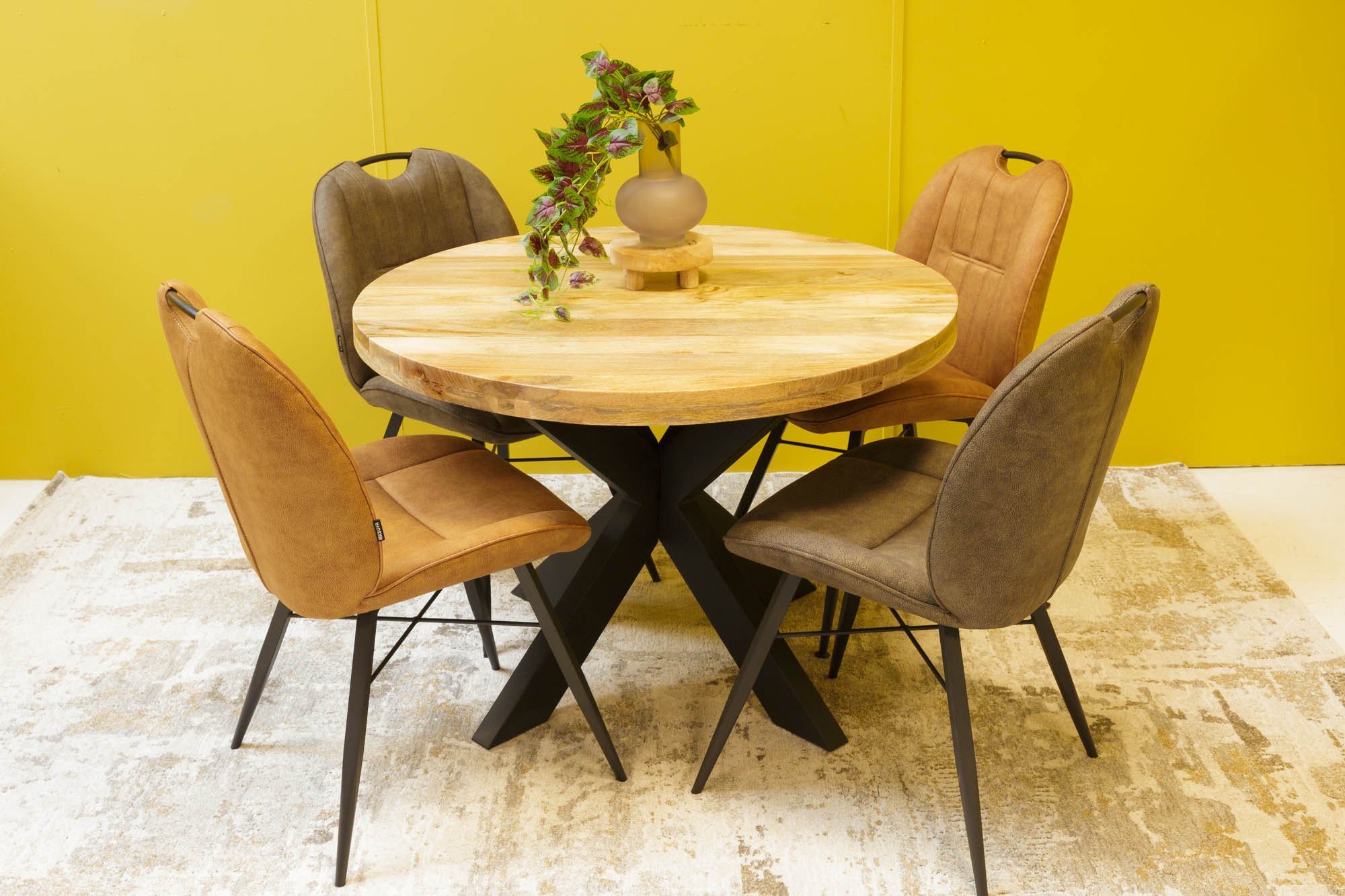Ronde eettafel met vier stoelen voor de gele wand van de showroom